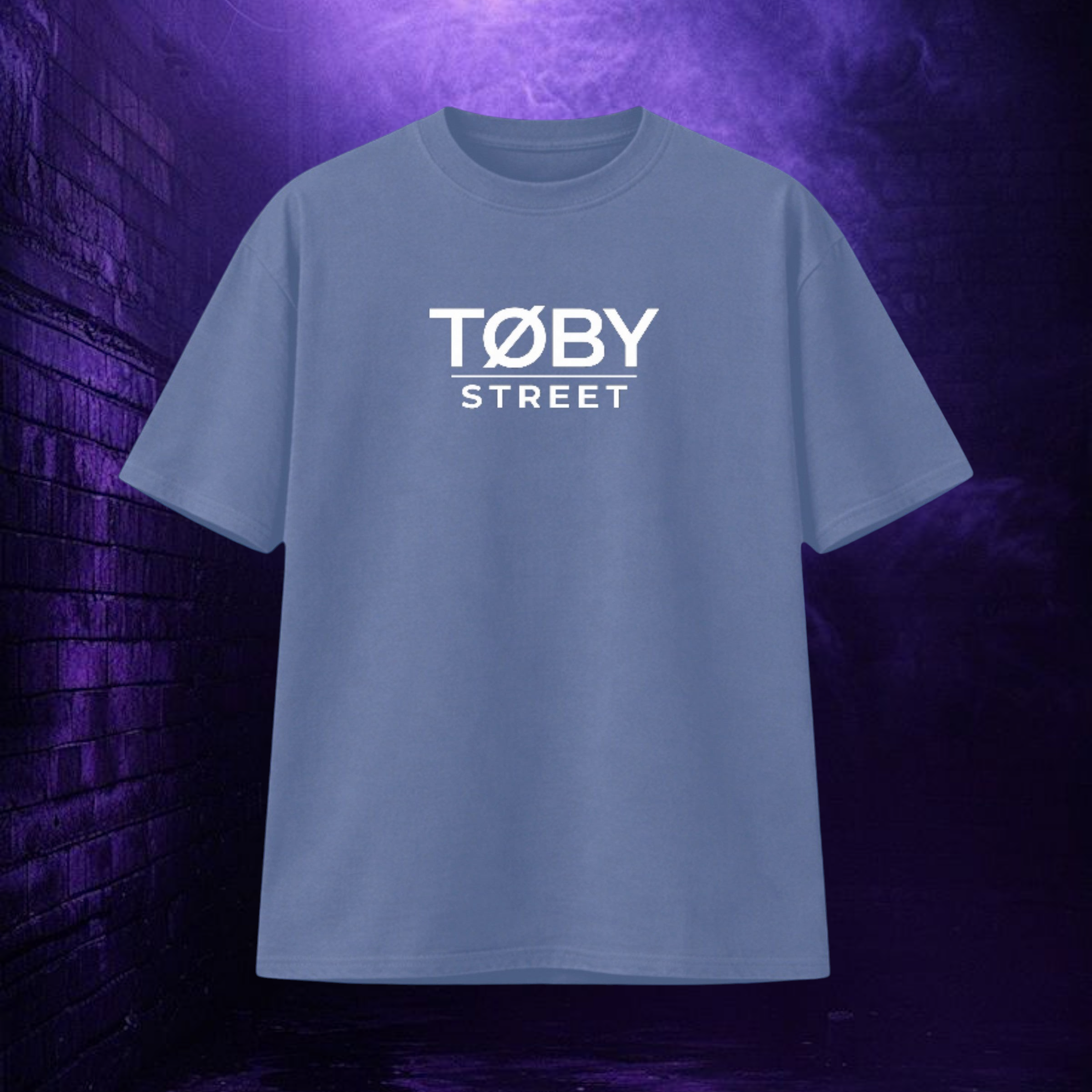 Camiseta oversize azul de TØBY STREET con logotipo blanco estampado en el pecho sobre fondo de pared de ladrillo